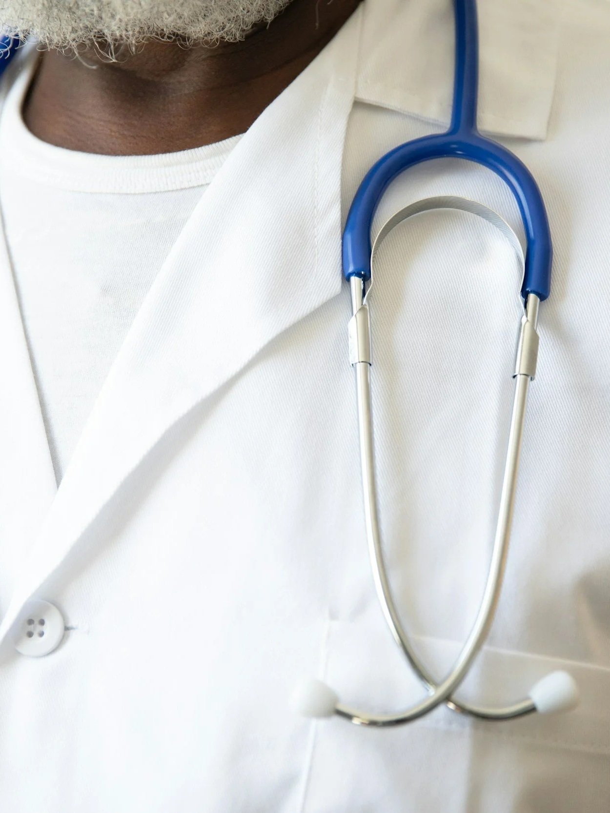 Close-up of a healthcare professional wearing a white coat with a blue and silver stethoscope around their neck.