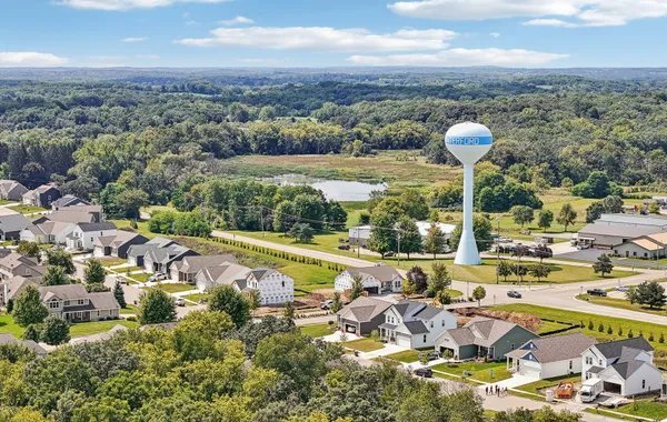 Suburban neighborhood with single-family homes and a water tower in a green landscape under a partly cloudy sky.