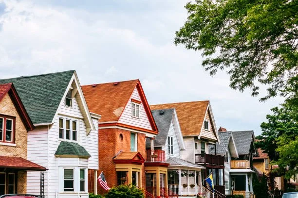 Line of colorful Craftsman-style houses with porches, in a neighborhood with trees and a cloudy sky.