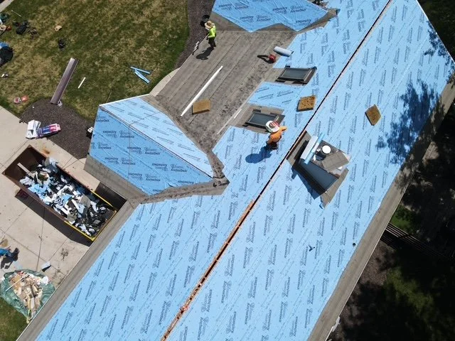 Aerial view of a building under construction with blue roofing material, workers, and construction tools.