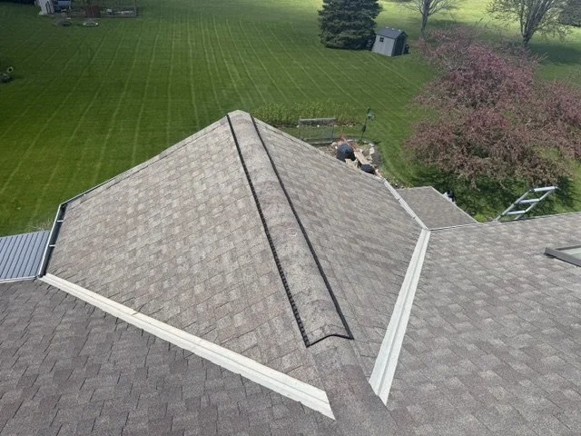 Aerial view of a house roof with a nearby backyard, trees, and a garden shed.