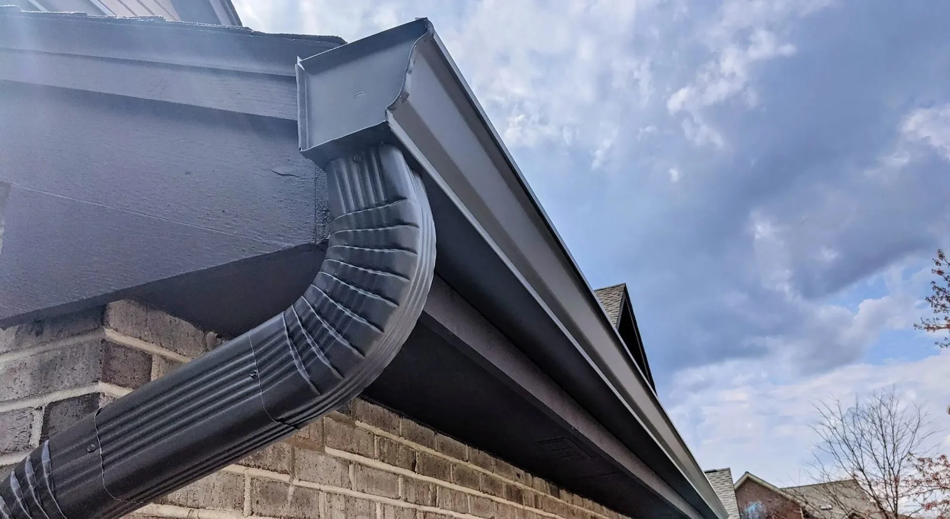 Black seamless gutter and downspout installation on brick home by lion guard roofing