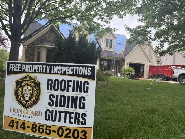A yard with a house undergoing roofing repairs and a sign advertising free property inspections and roofing services, including siding and gutters, with a phone number.