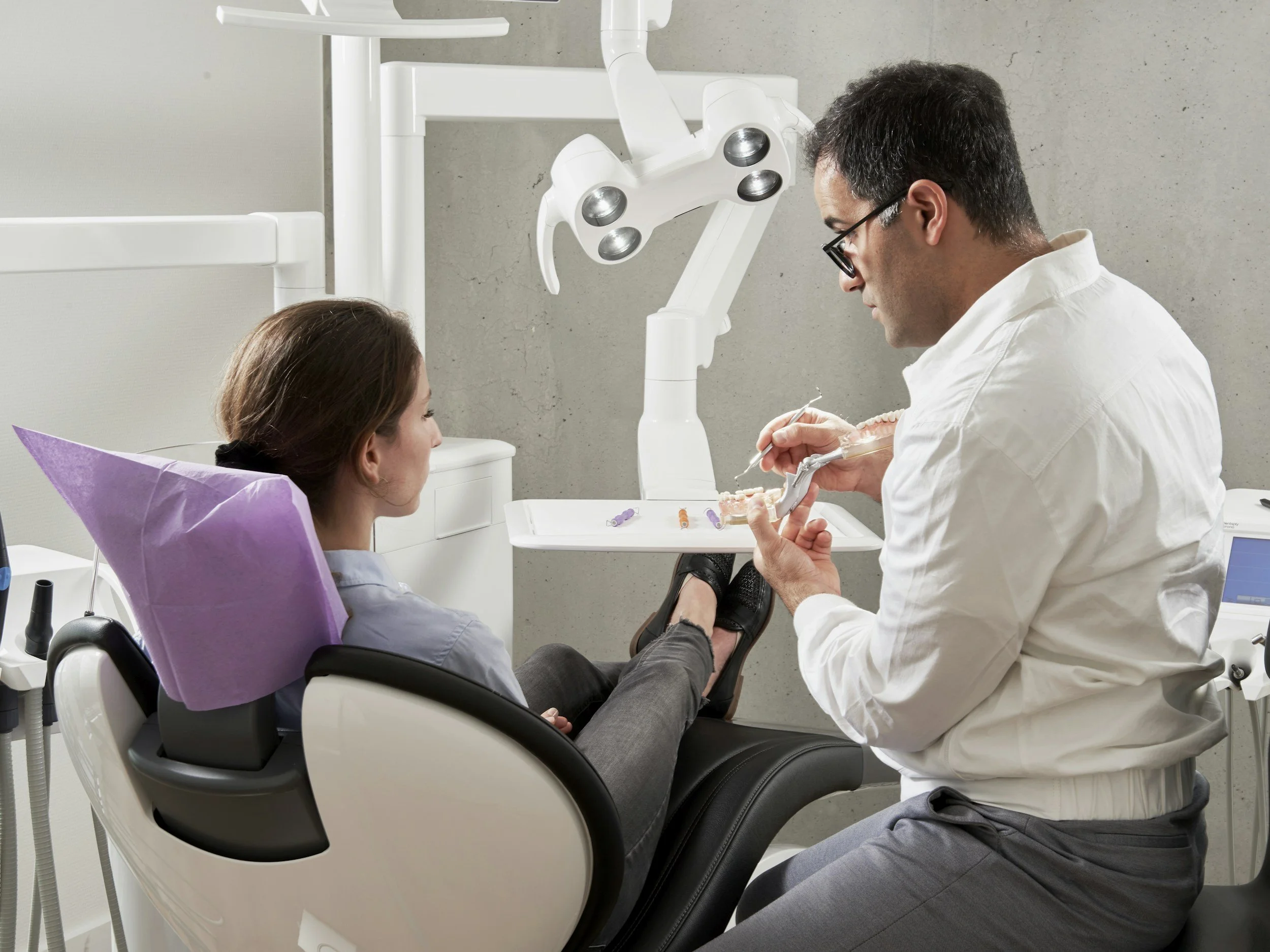Dentist examining a patient's teeth in a dental clinic, with dental equipment and a chair in the background.