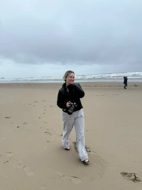 Oregon elopement photographer holding a camera on the beach at Ecola State Park along the Oregon Coast.