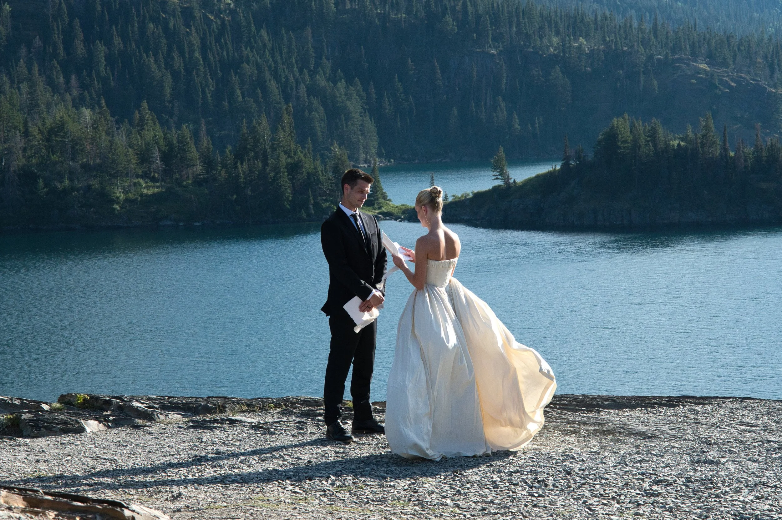 Couple reading vows during their Montana elopement at St. Mary Lake in Glacier National Park, with mountains in the background.