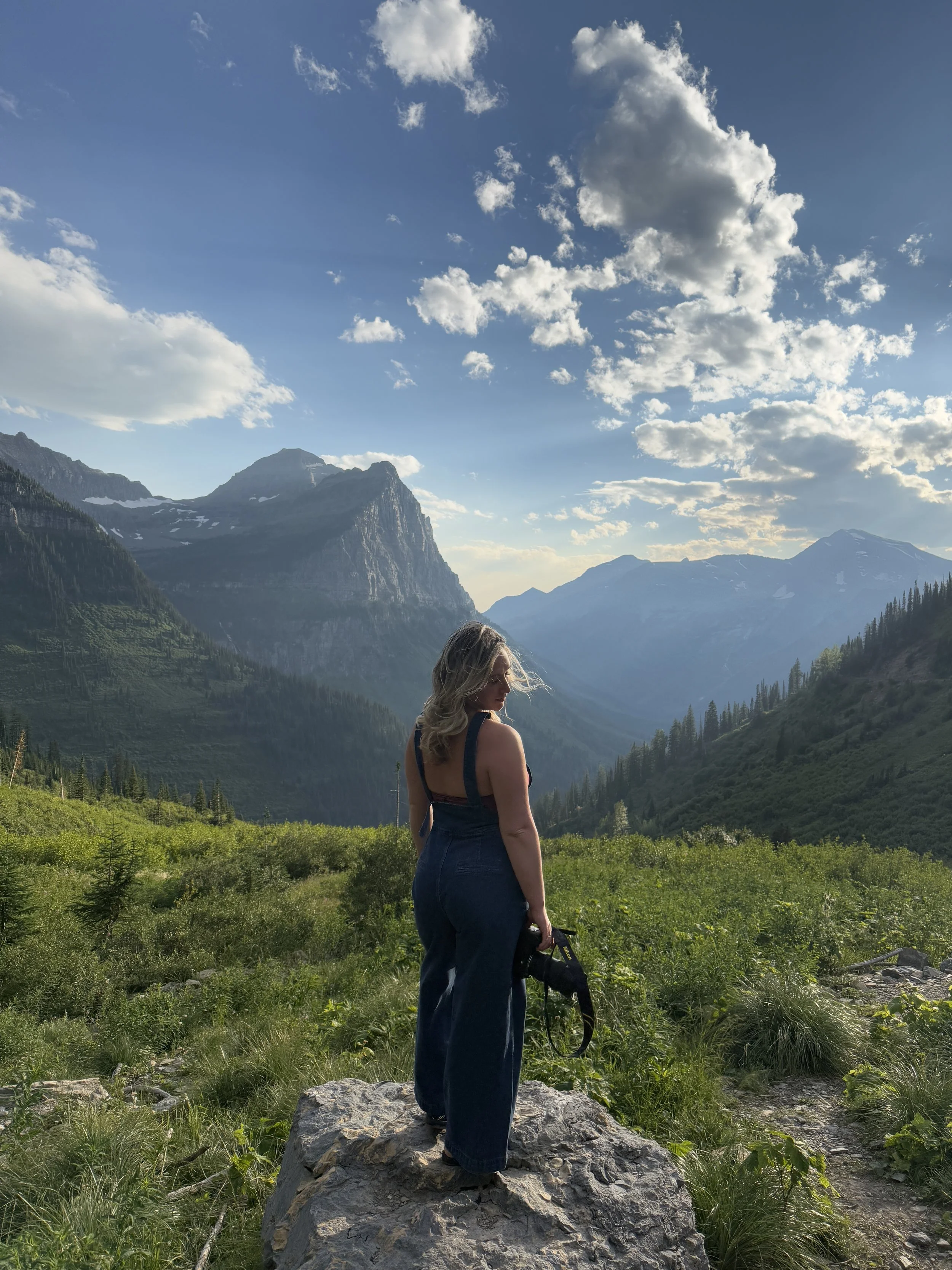 Montana elopement photographer holding a camera in West Glacier near Going-to-the-Sun Road with mountains in the background.
