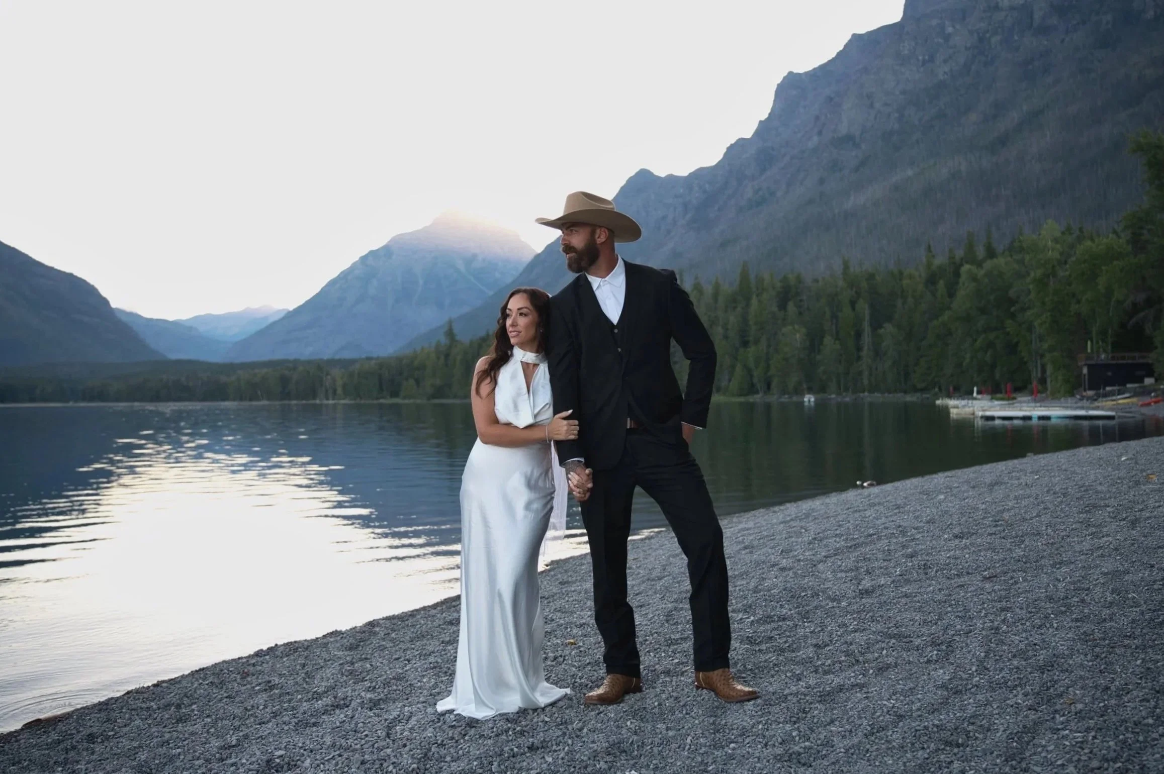 Couple embracing at sunrise during their elopement at Lake McDonald, with calm lake waters and mountains in the background.