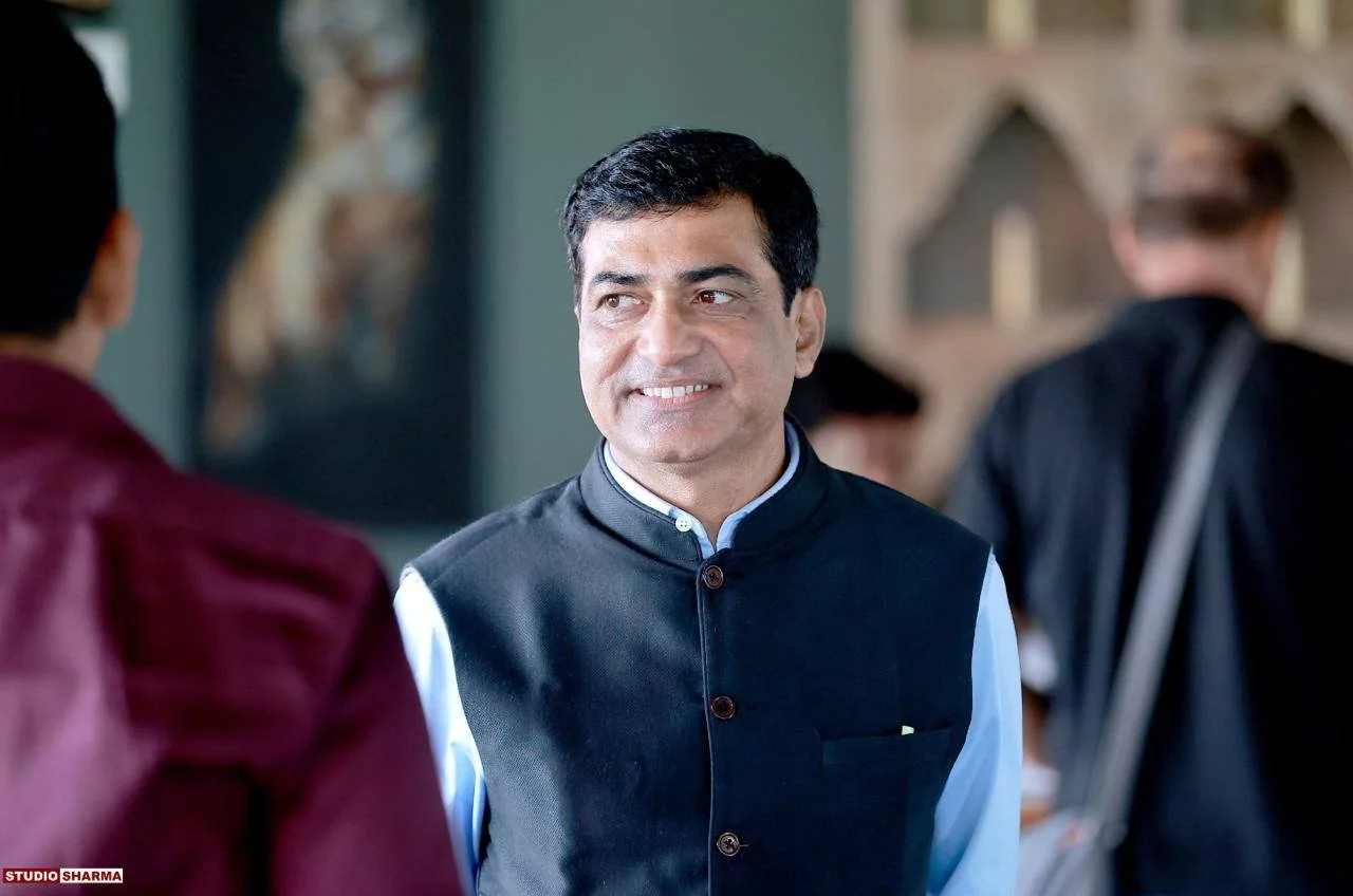 A man smiling and talking to another person at a social gathering, with other people in the background.