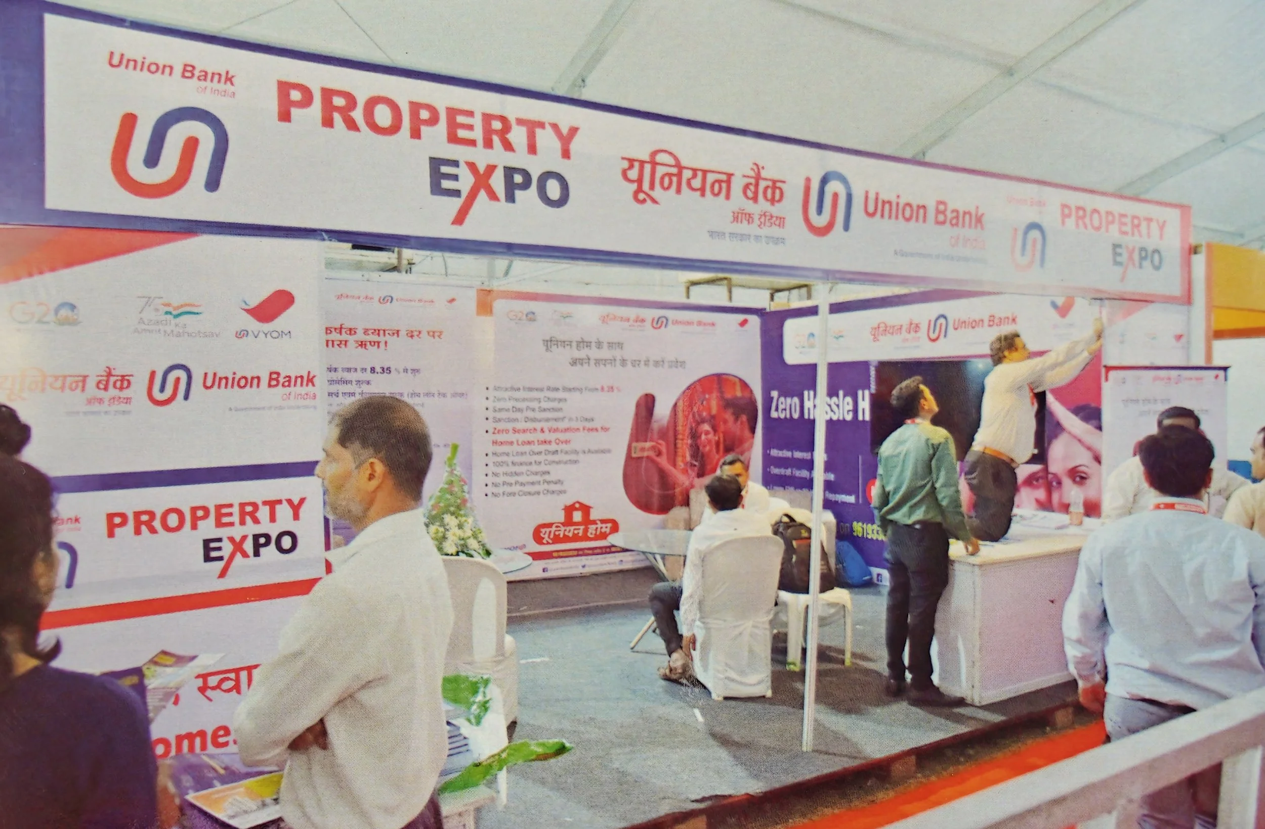People attending a property expo booth of Union Bank of India with banners displaying 'PROPERTY EXPO' and promotional information in Hindi.