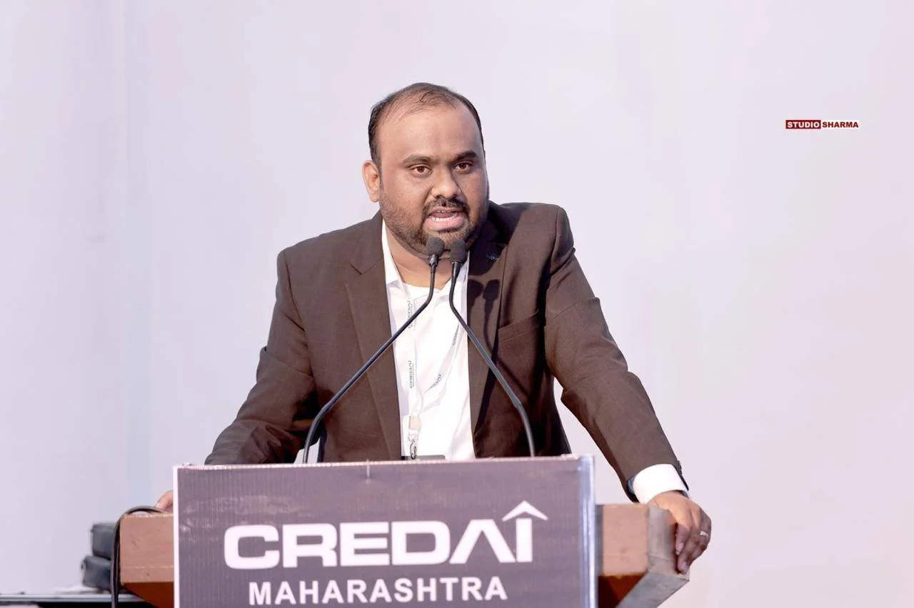 Man in a dark suit speaking at a podium with a sign that reads 'CREDĀ Maharashtra', in front of a plain white background.