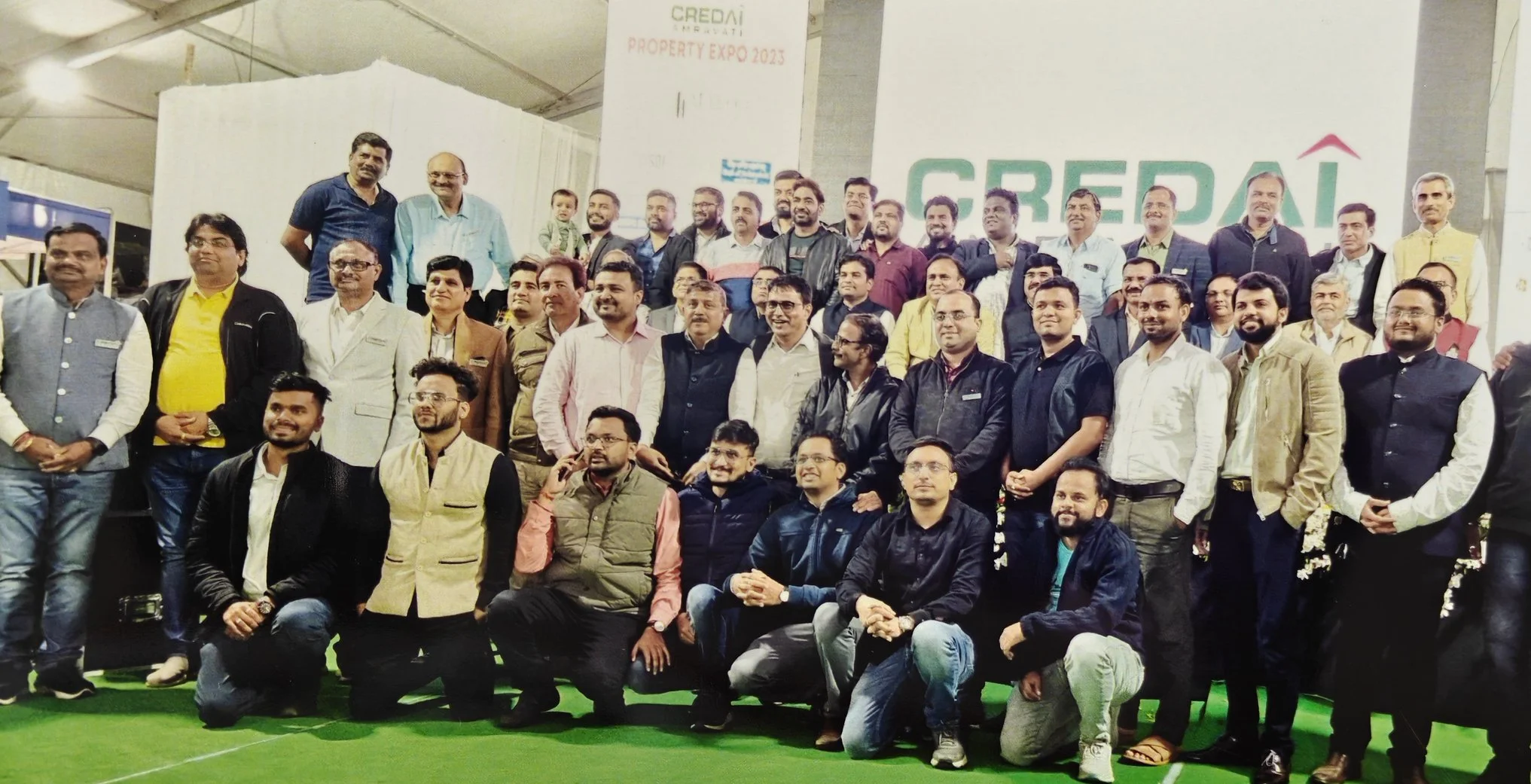 Group of men and women gathered at an indoor event with a large sign reading 'CREDAI' and 'PROPERTY EXPO 2023' in the background.