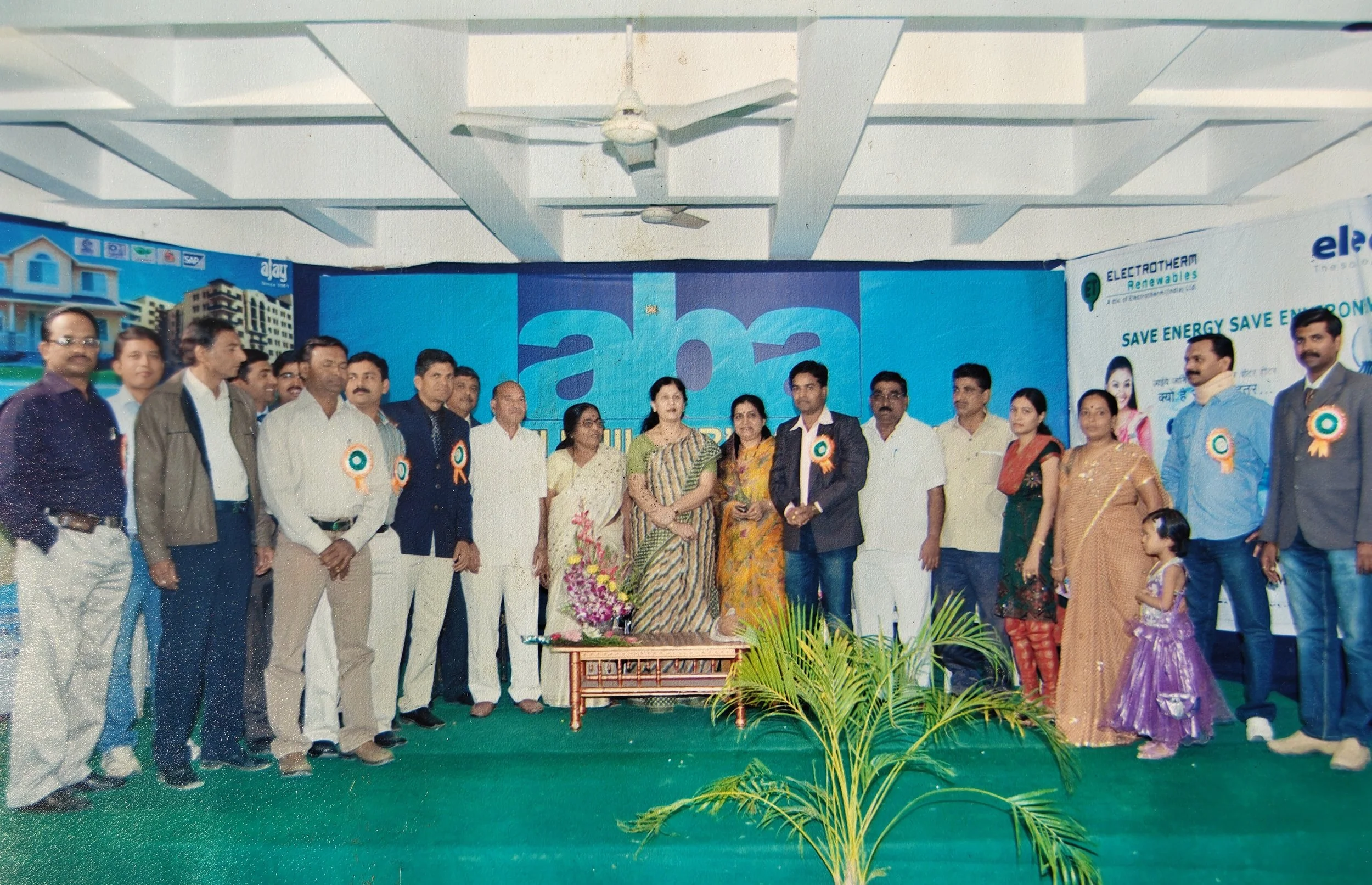 Group of people standing on stage during an event celebrating energy conservation, with banners promoting energy saving and a potted plant in the foreground.
