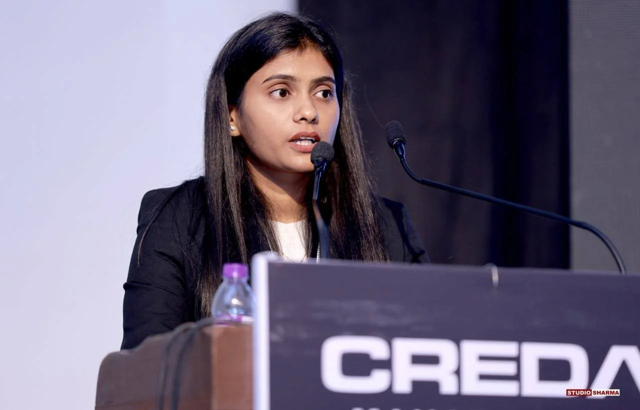 A woman speaking at a podium during a conference or event, with a sign that reads 'CREDA' in front of her.