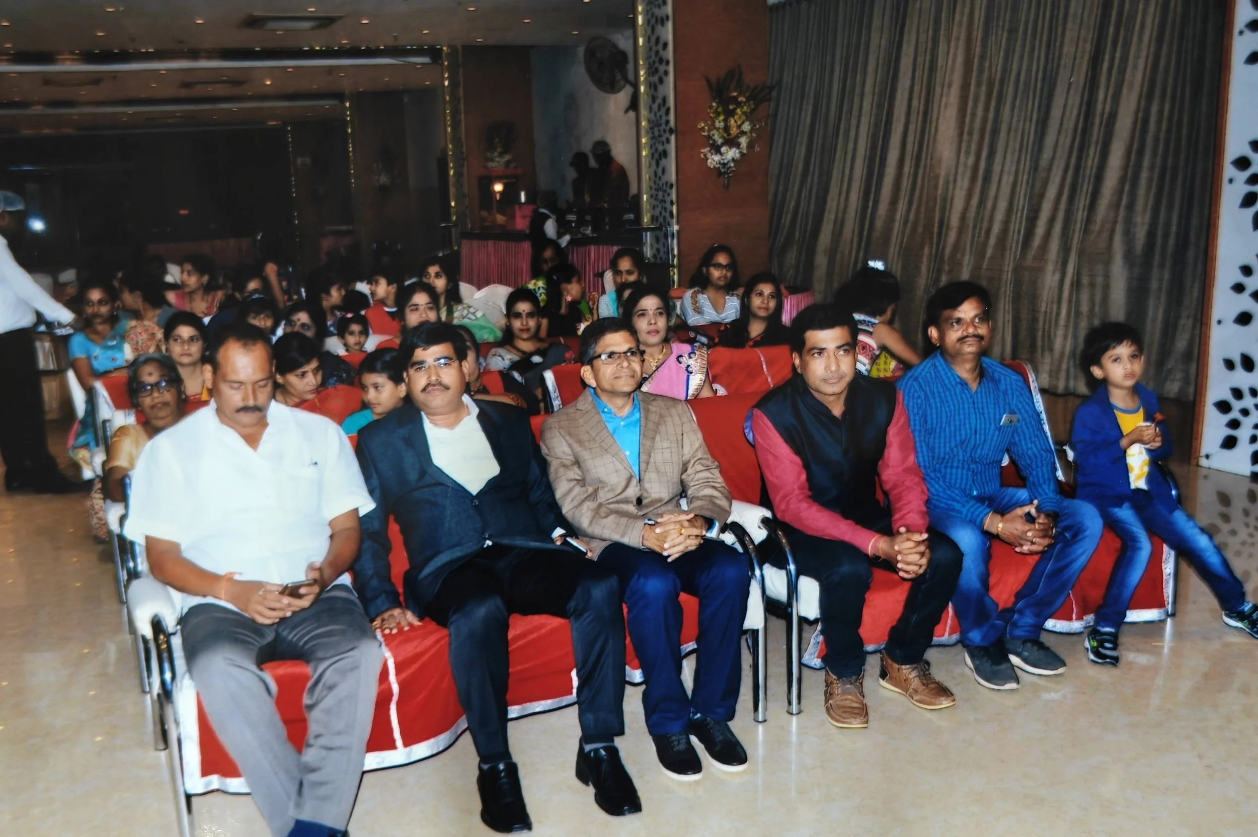 An audience sitting in a decorated hall, including children and adults, at a formal event or celebration.