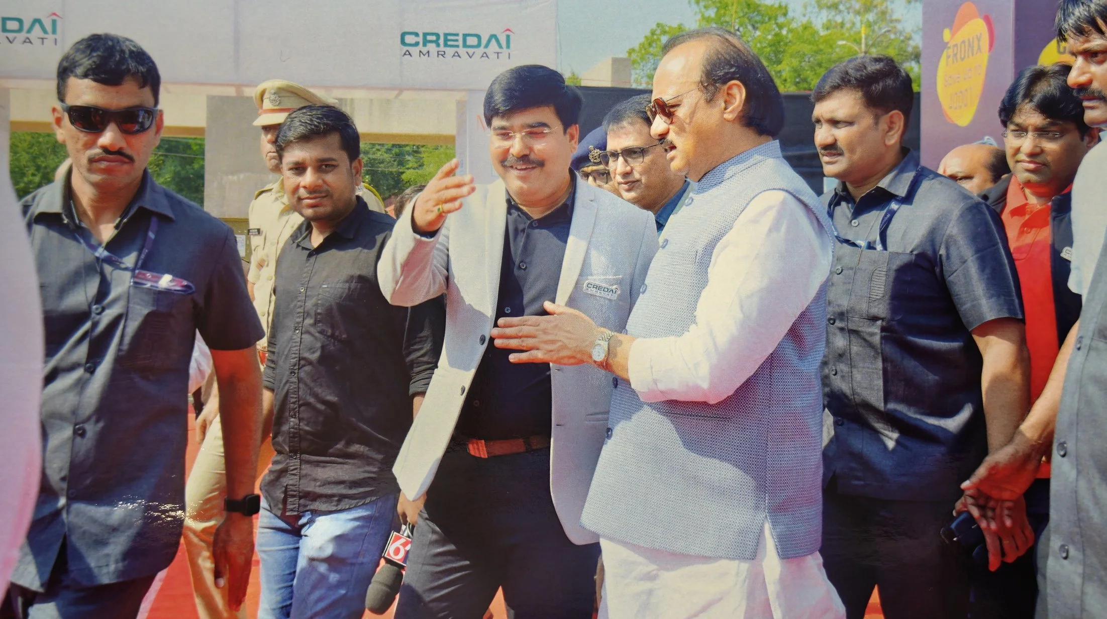 Group of men, including a man in traditional Indian attire and another in a blazer with a 'Credai' badge, engaging in conversation outdoors at a formal event.