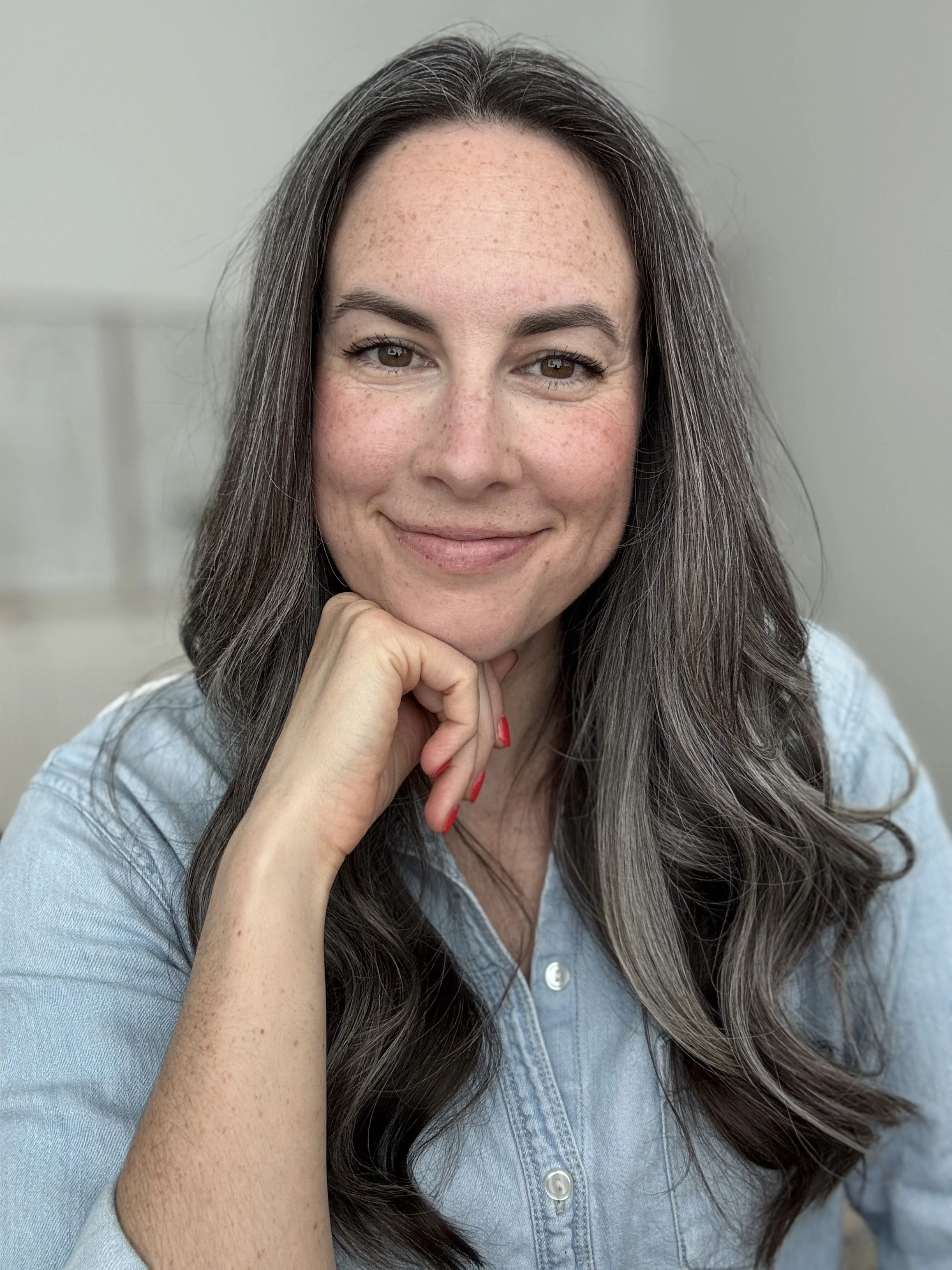 A picture of Kate smiling while resting her chin on her hand. Kate offers eating disorder therapy in Raleigh, NC for women navigating trauma, body concerns & more. Reach out today to start healing with Kate.