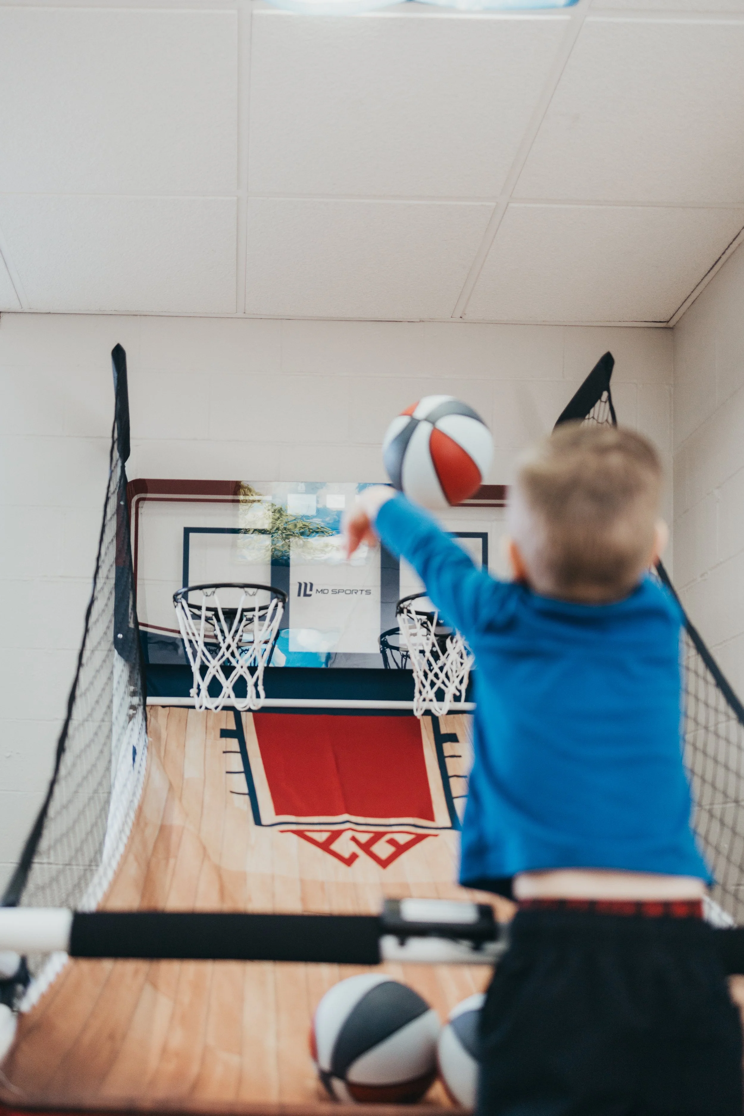 Child playing an indoor basketball game with a mini basketball hoop, shooting a ball into the hoop.