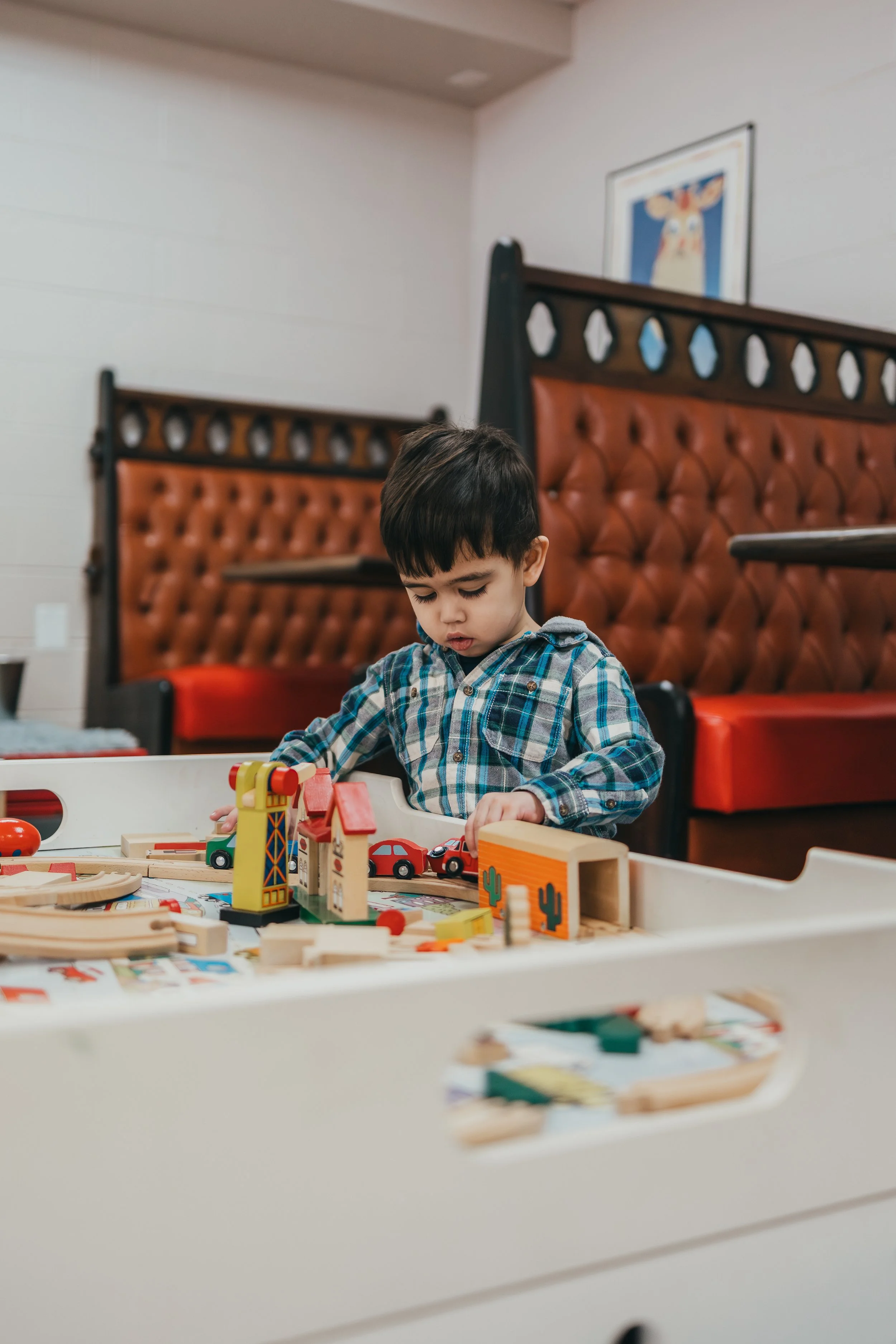 A young boy playing with wooden toy cars and train set in a restaurant.