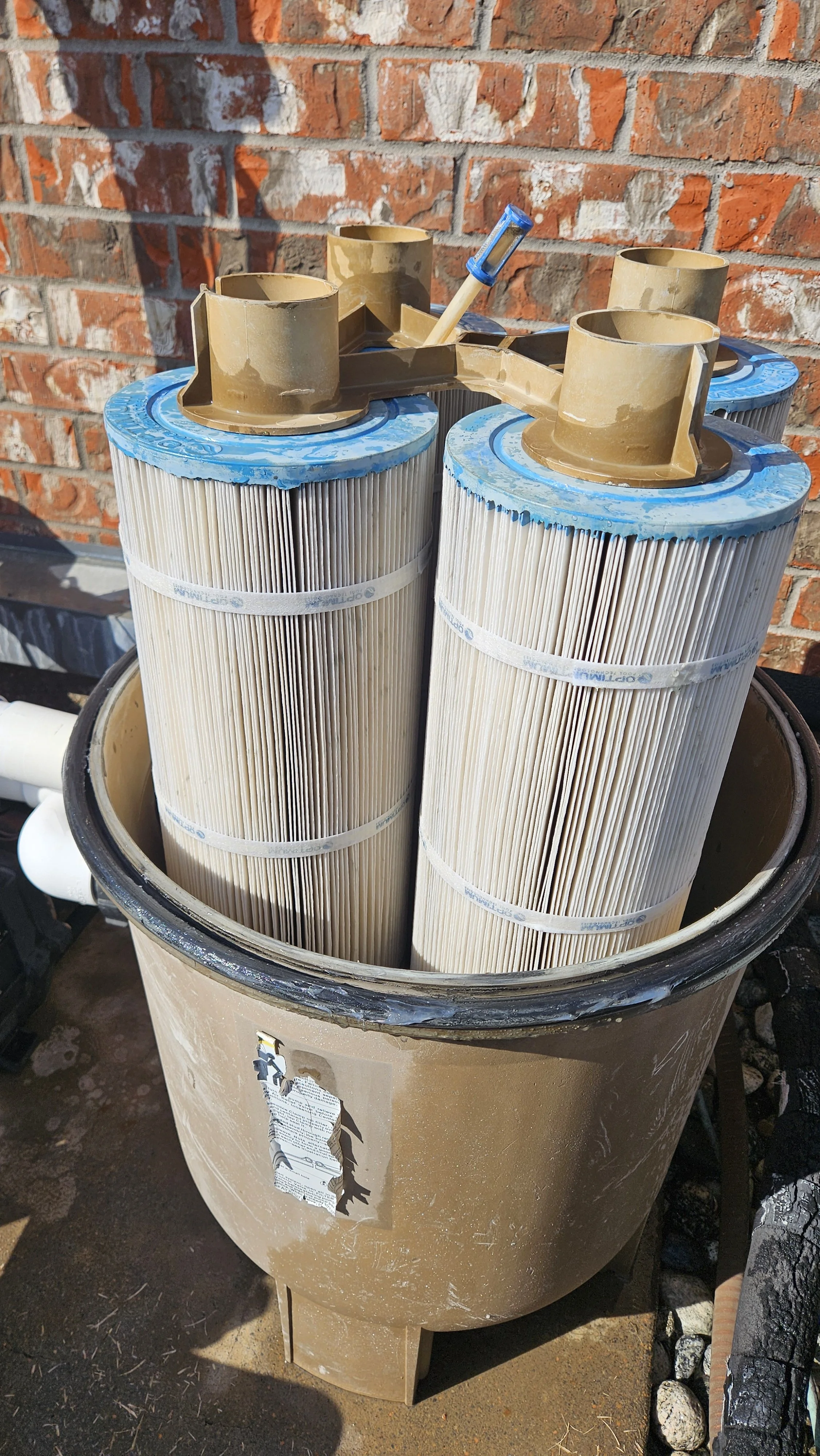 Pool filter cartridges stored in a large container with a brick wall in the background.