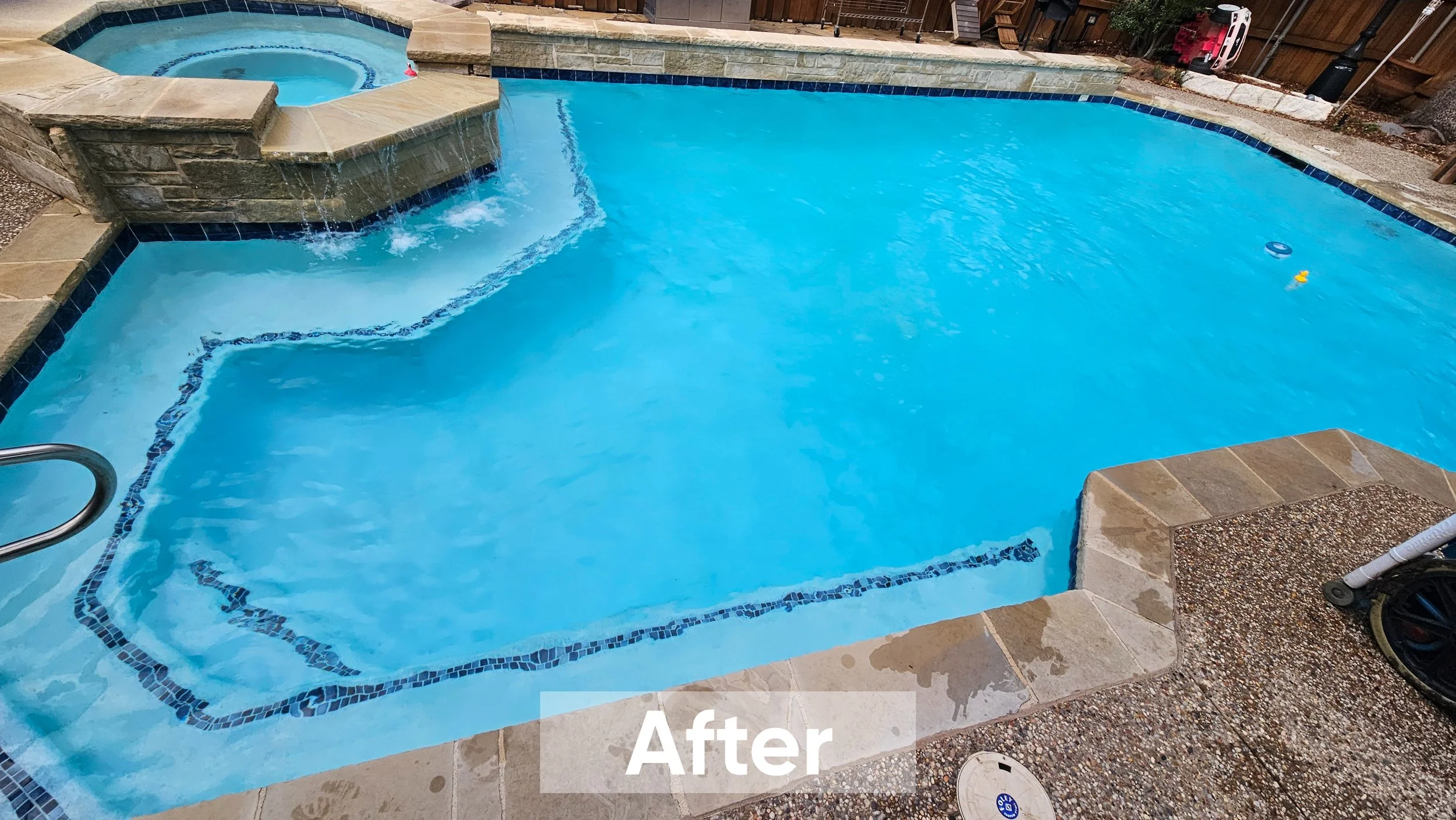 Clean and tidy backyard swimming pool with a hot tub, surrounded by a stone deck, with pool toys floating on the water.