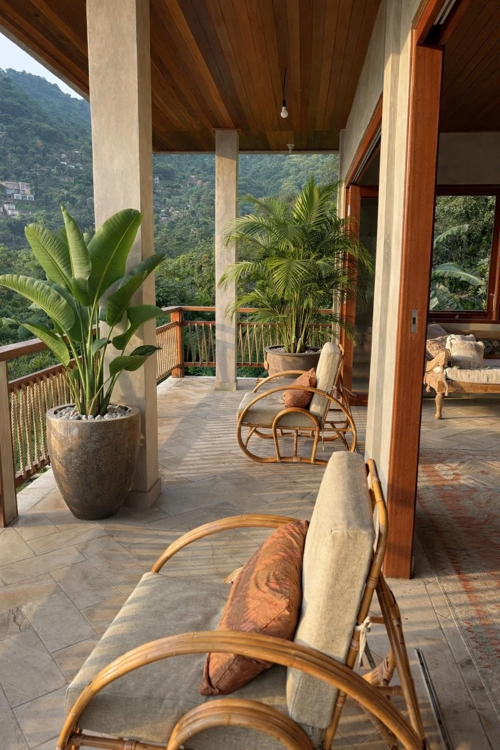 A covered balcony with wicker chairs, large potted plants, and a scenic mountain view in the background.