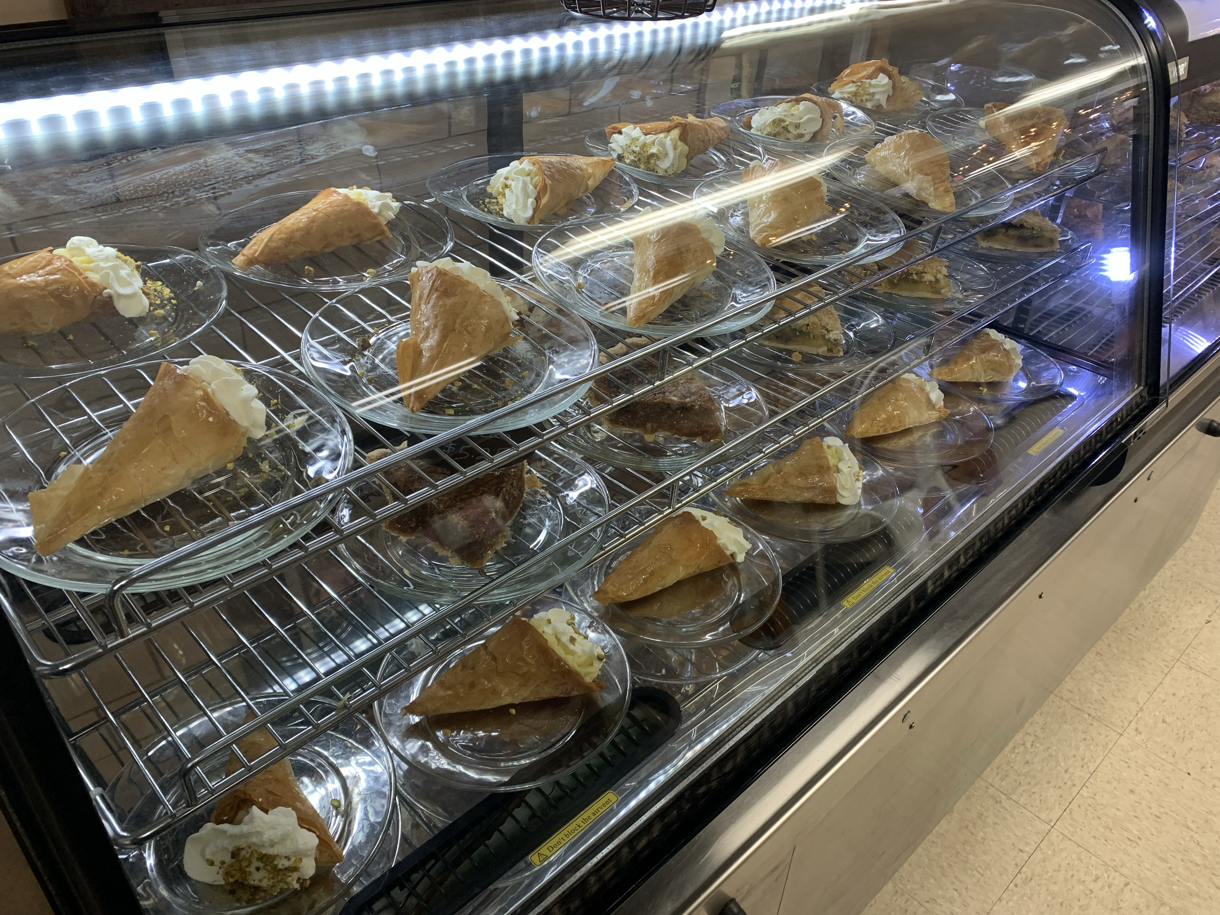 Display case with multiple plates of cannoli, some with filling and some empty, inside a bakery or cafe.