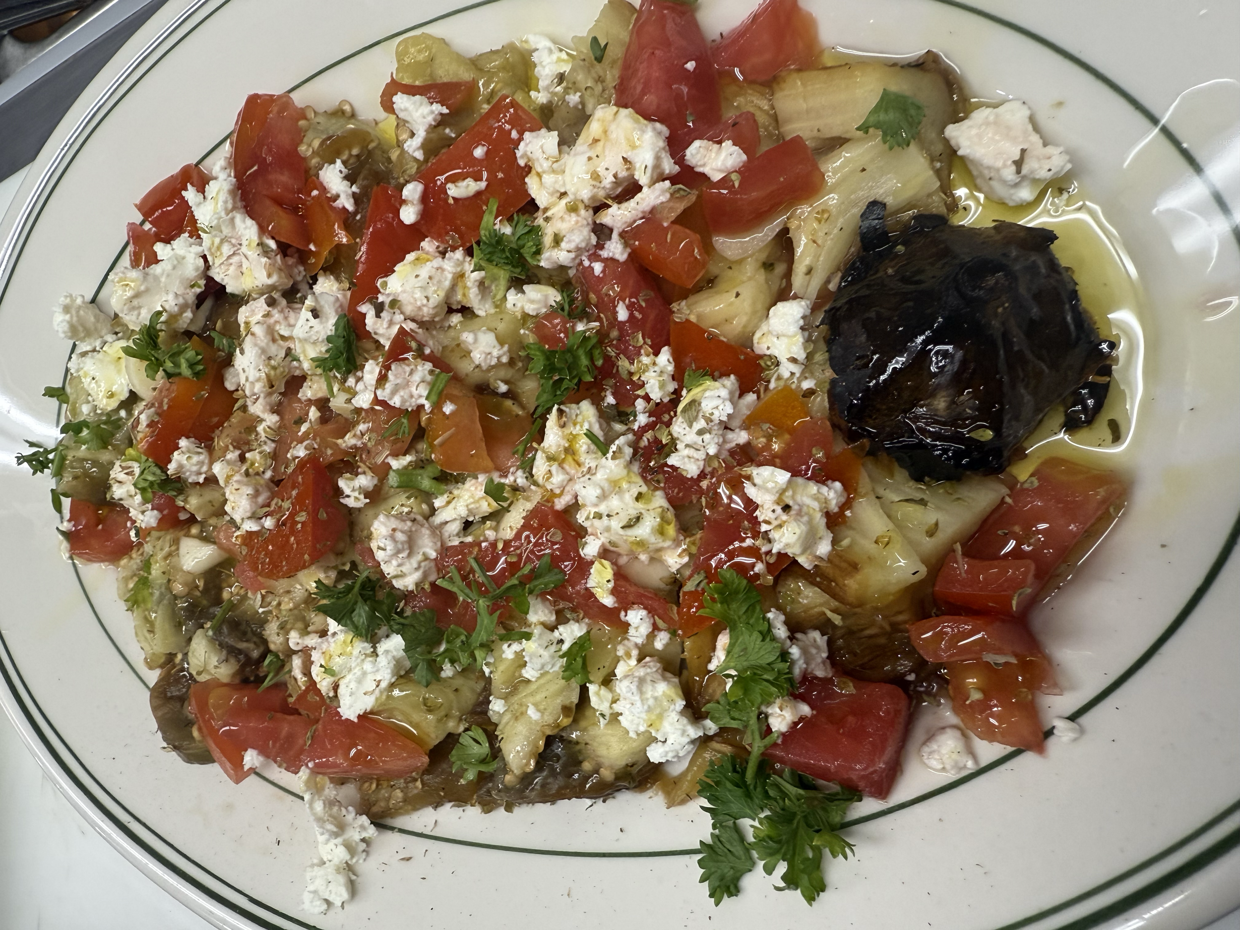 A plate of roasted vegetables topped with crumbled cheese and garnished with parsley, featuring eggplant, tomatoes, and red bell peppers.