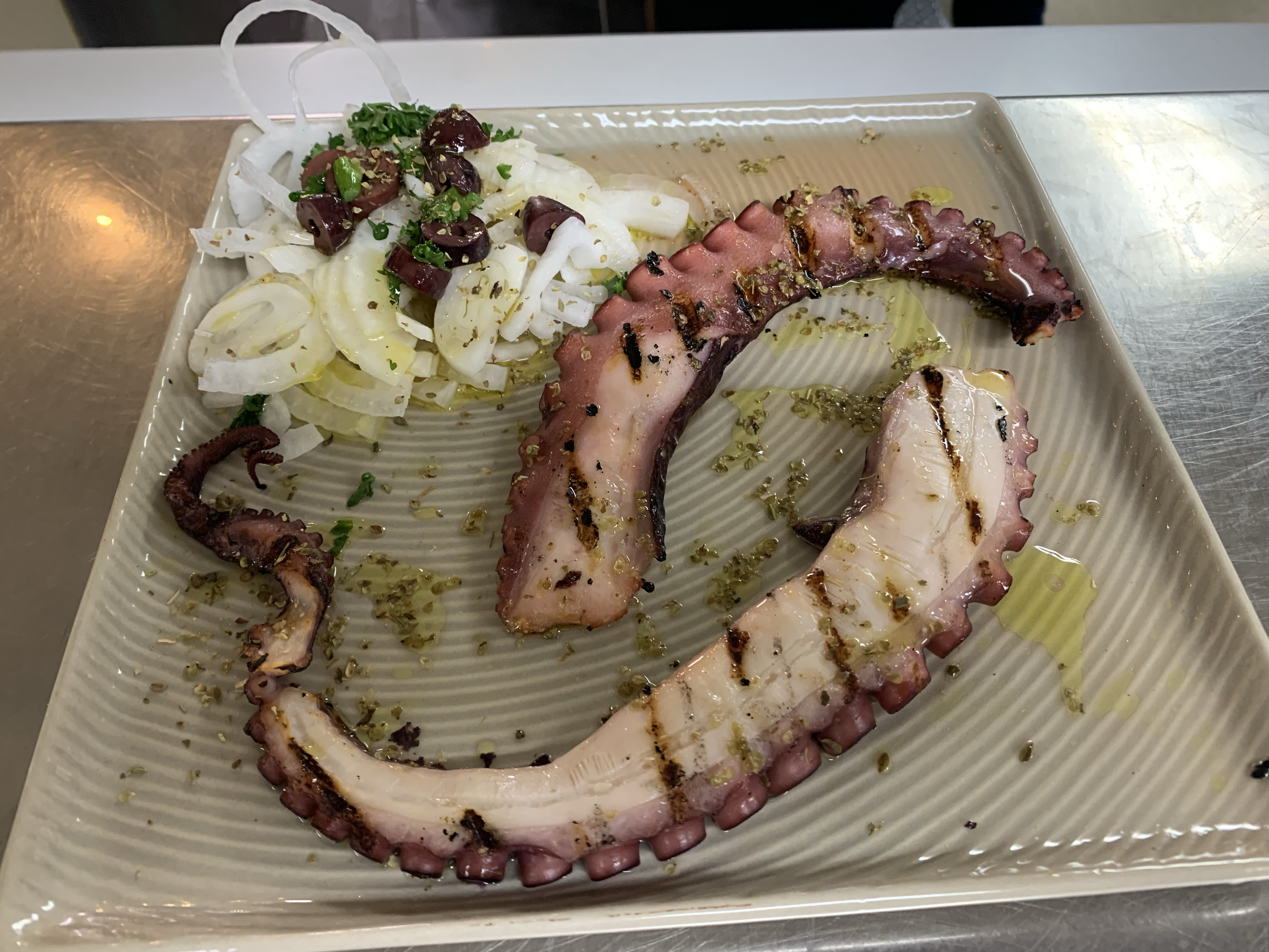 Grilled octopus tentacles on a plate with a side of white cabbage salad with olives and herbs, drizzled with olive oil.