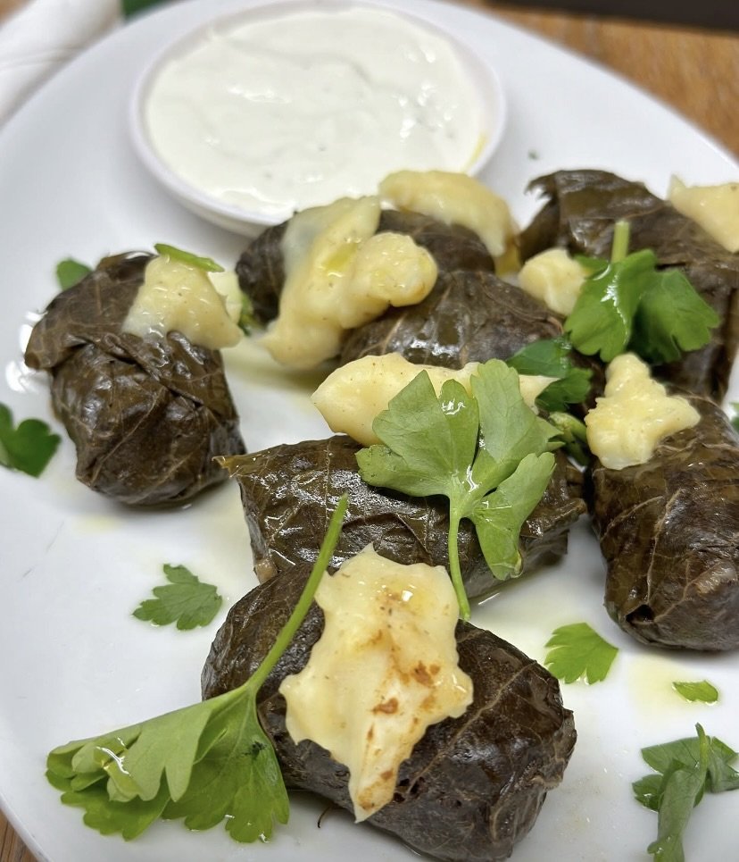 Stuffed grape leaves with a dollop of cream or yogurt and fresh parsley on a white plate.