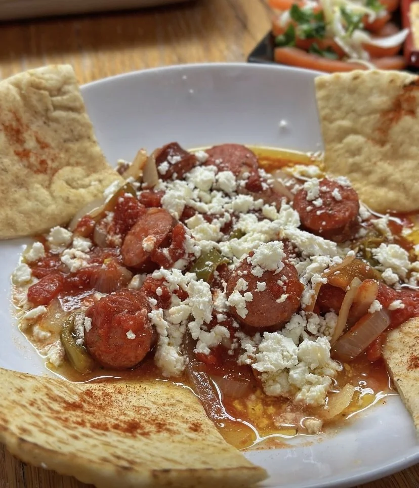 Plate of Mexican dish with beef or sausage, tomato, and cheese, garnished with papas or tostadas, and a side salad in the background.