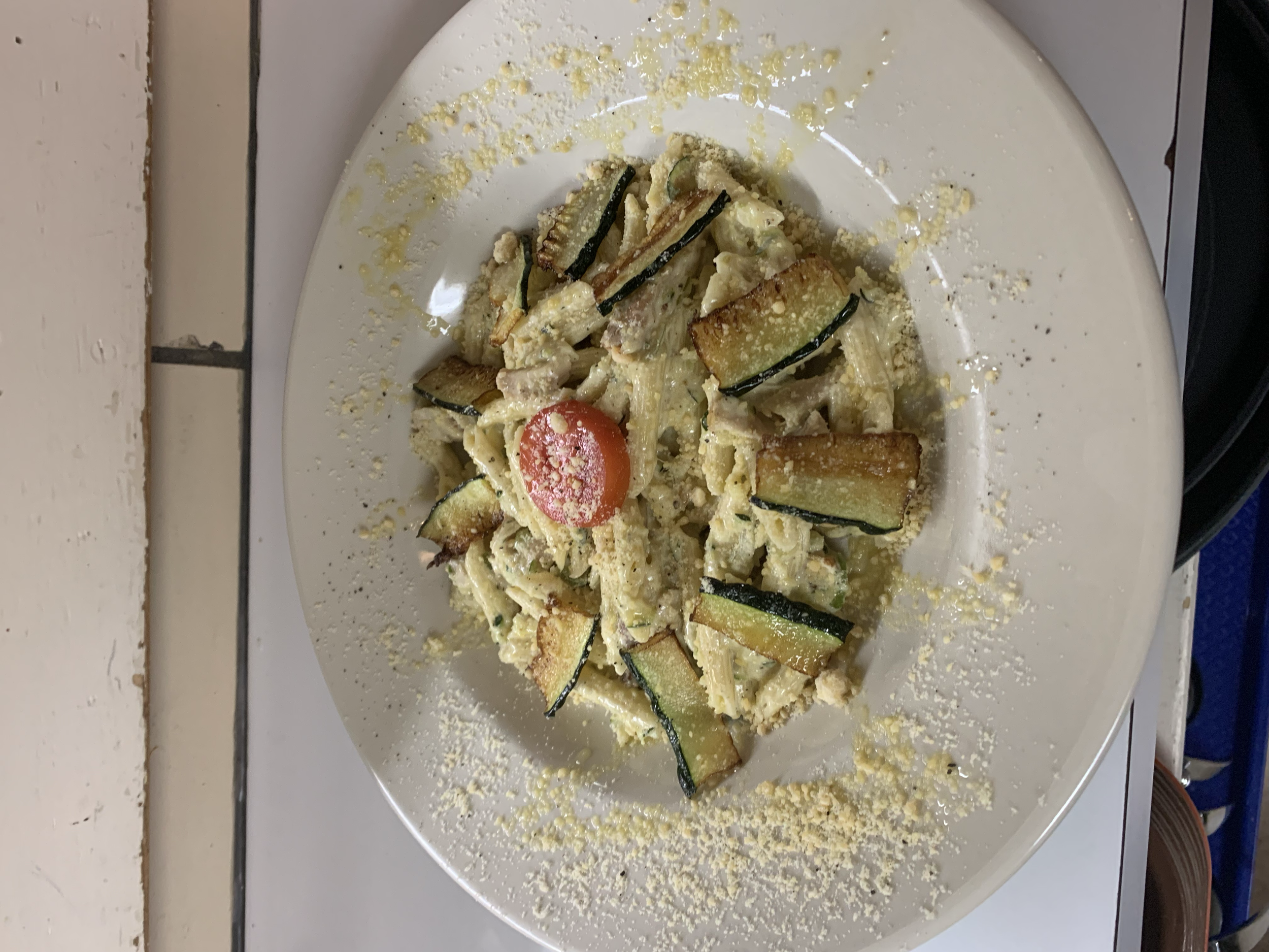 A plate of pasta with zucchini, cherry tomato, grated cheese, and a creamy sauce.