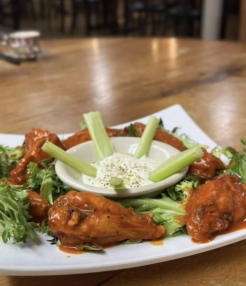 Plate of buffalo chicken wings with celery sticks and dipping sauce on a wooden table.