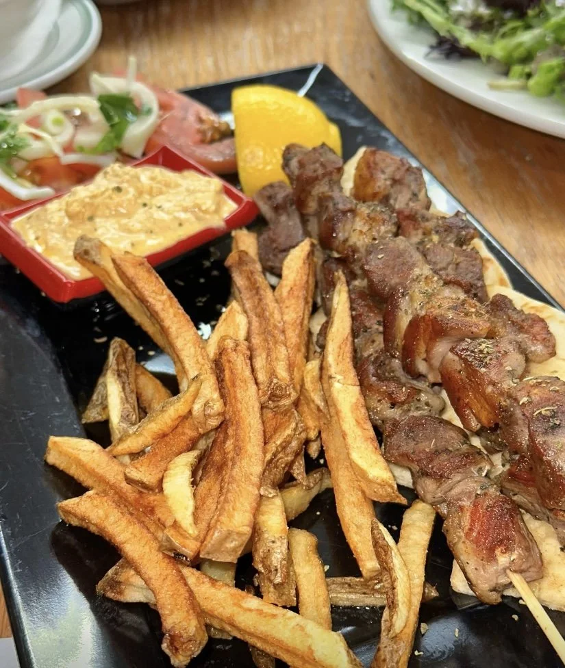 Plate of French fries, grilled meat skewers, a lemon wedge, a small bowl of fried onion rings, and a salad with greens and tomato slices.