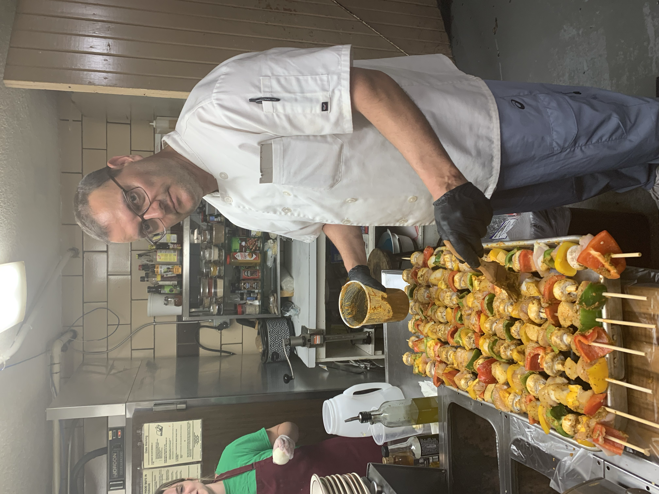 Chef preparing skewers with vegetables and meat in a kitchen.
