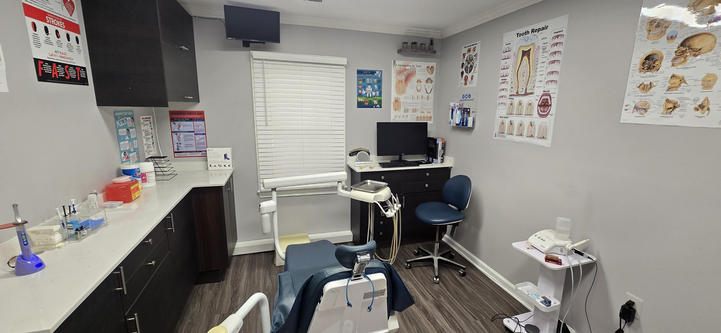 dentist exam room and dentist chair, inside dentist office.  The image has dental posters on the wall and dental equipment.