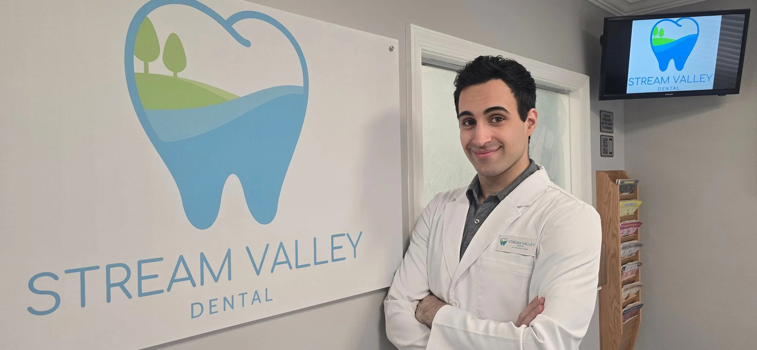 Dentist standing in the waiting room of Stream Valley Dental, in front of the Stream Valley Dental sign