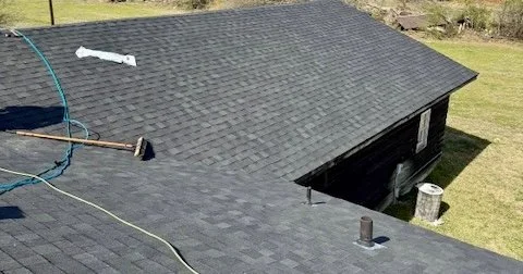 View of a rooftop with black shingles, a hose and broom lying on it, and a chimney.