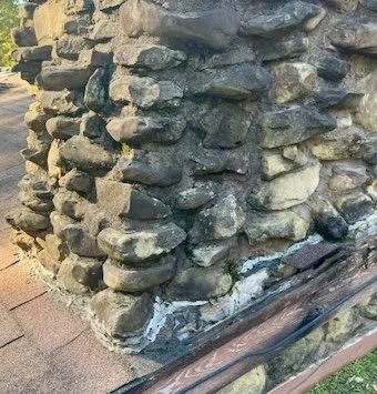 Close-up of a stone corner wall with visible mortar, next to a wooden railing and a section of brick pavement.