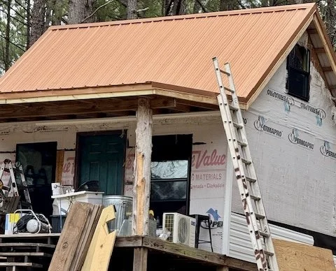House under construction with a steep orange roof, ladder leaning against the front, and construction materials on the porch.