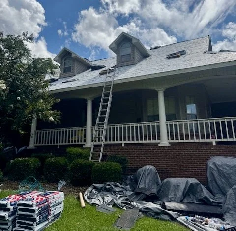 A large house with a front porch, two dormer windows, and a ladder leaning against the roof, possibly for roof maintenance or repair.