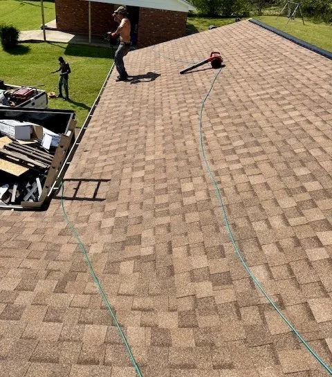 Person working on roof with roofing tools, two children playing on the lawn below.