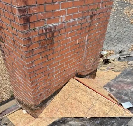 Close-up of a brick chimney with plywood sheets and construction materials around it.