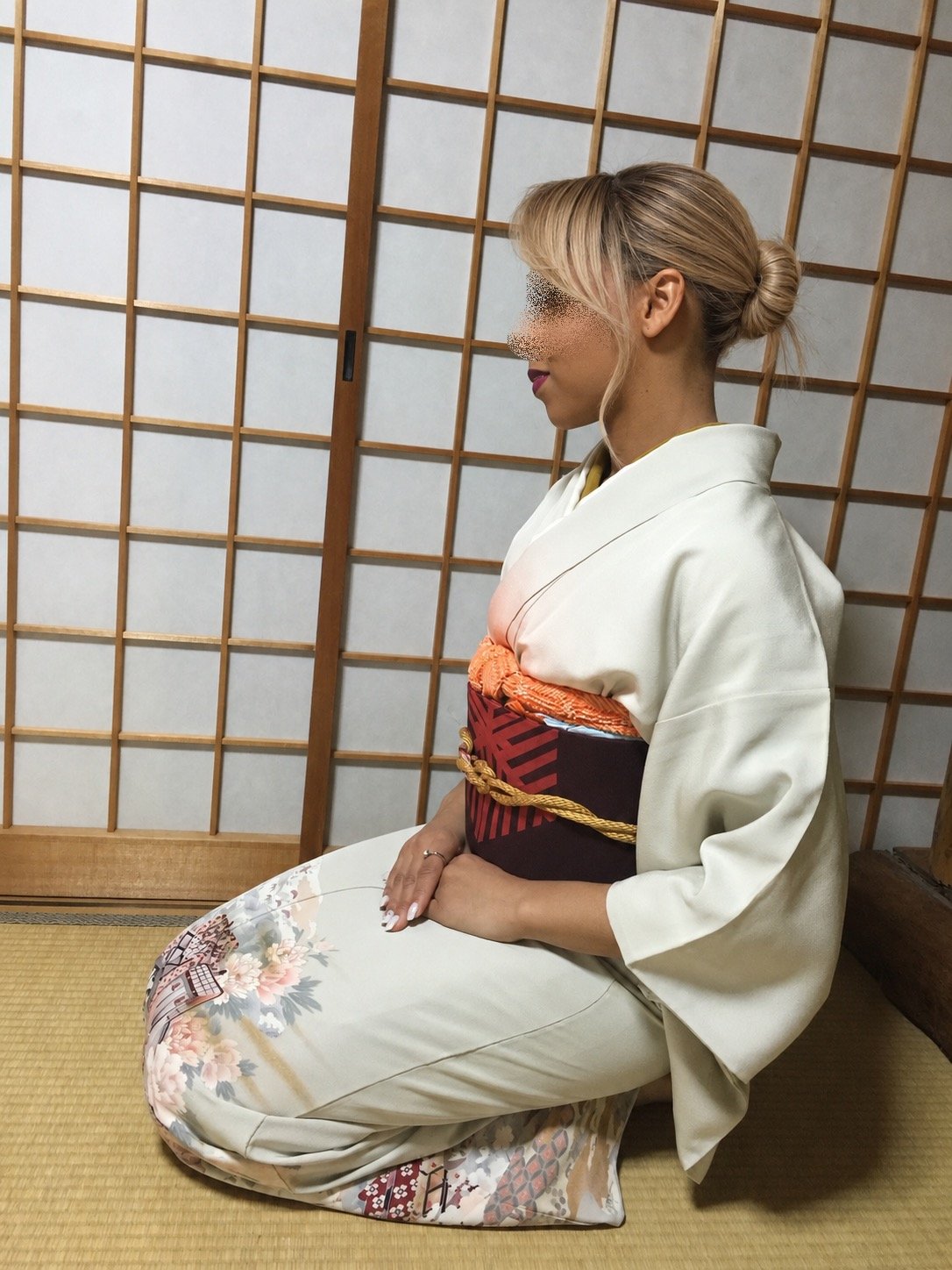 Woman in a white floral kimono and burgundy obi sitting on tatami flooring in a traditional Japanese room