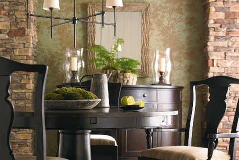 Dining room with a round wooden table, black chairs, a chandelier, and a wall with stone accents.