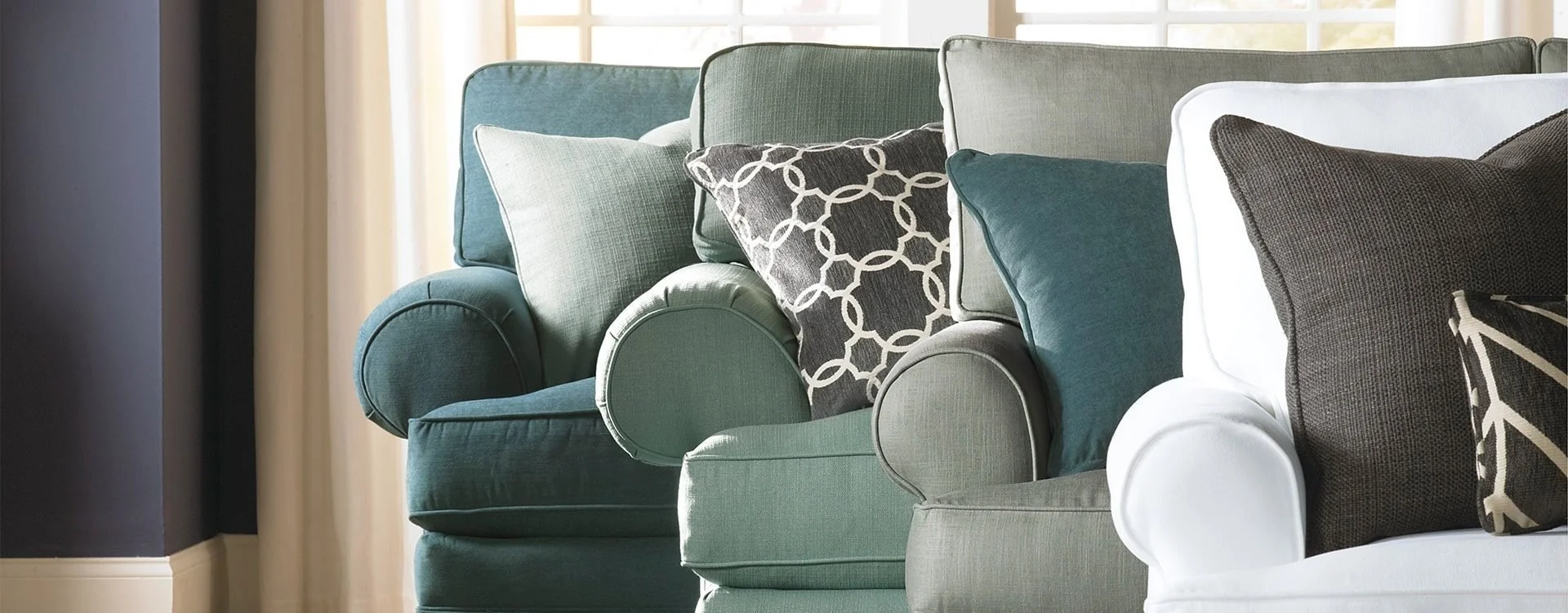 A row of sofas with throw pillows in living room near large windows with white curtains