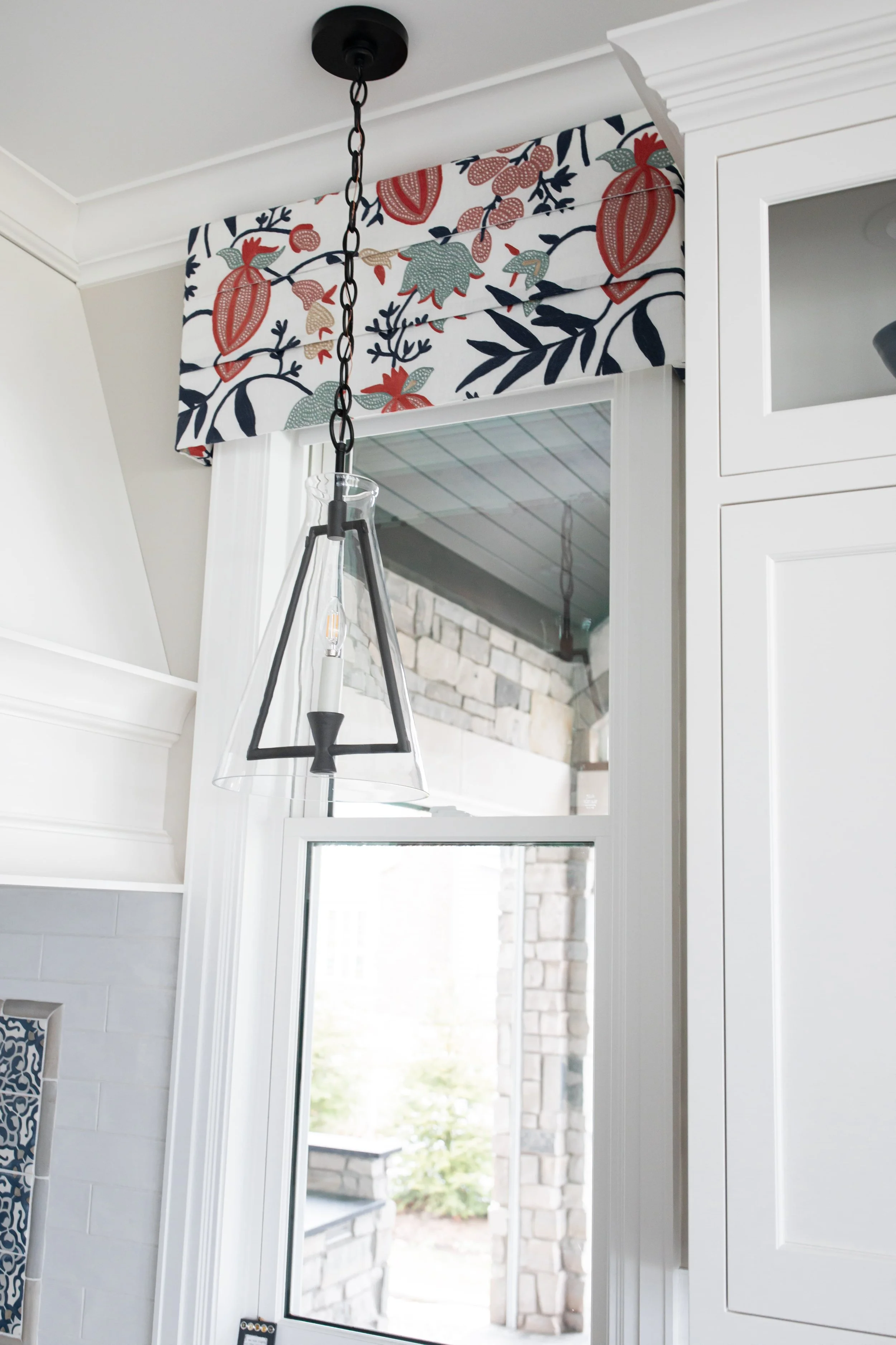 Custom kitchen window treatment with patterned fabric valance and pendant lighting, adding color and character to a lakeside interior design in Kalamazoo, Michigan.
