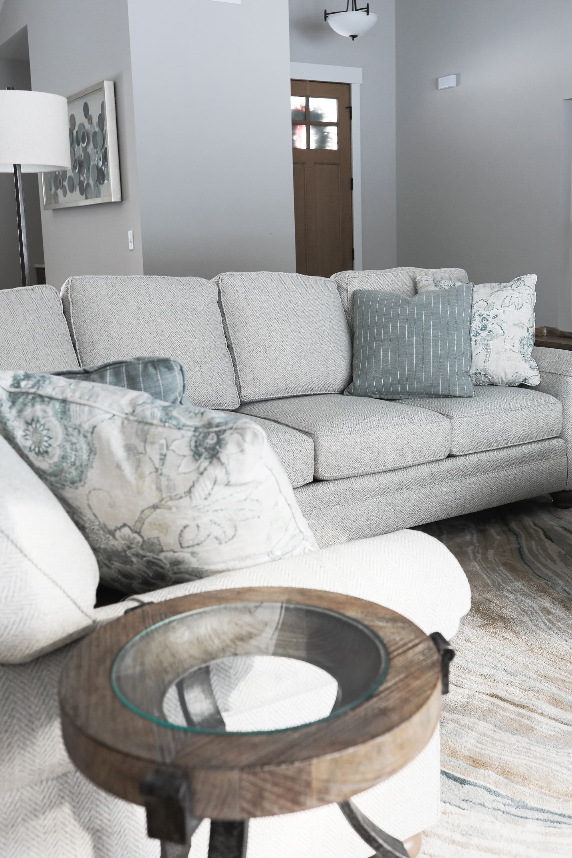 Neutral living room with textured sofa, patterned accent pillows in soft blue tones, wood and glass side table, and layered area rug in a calm, inviting space.