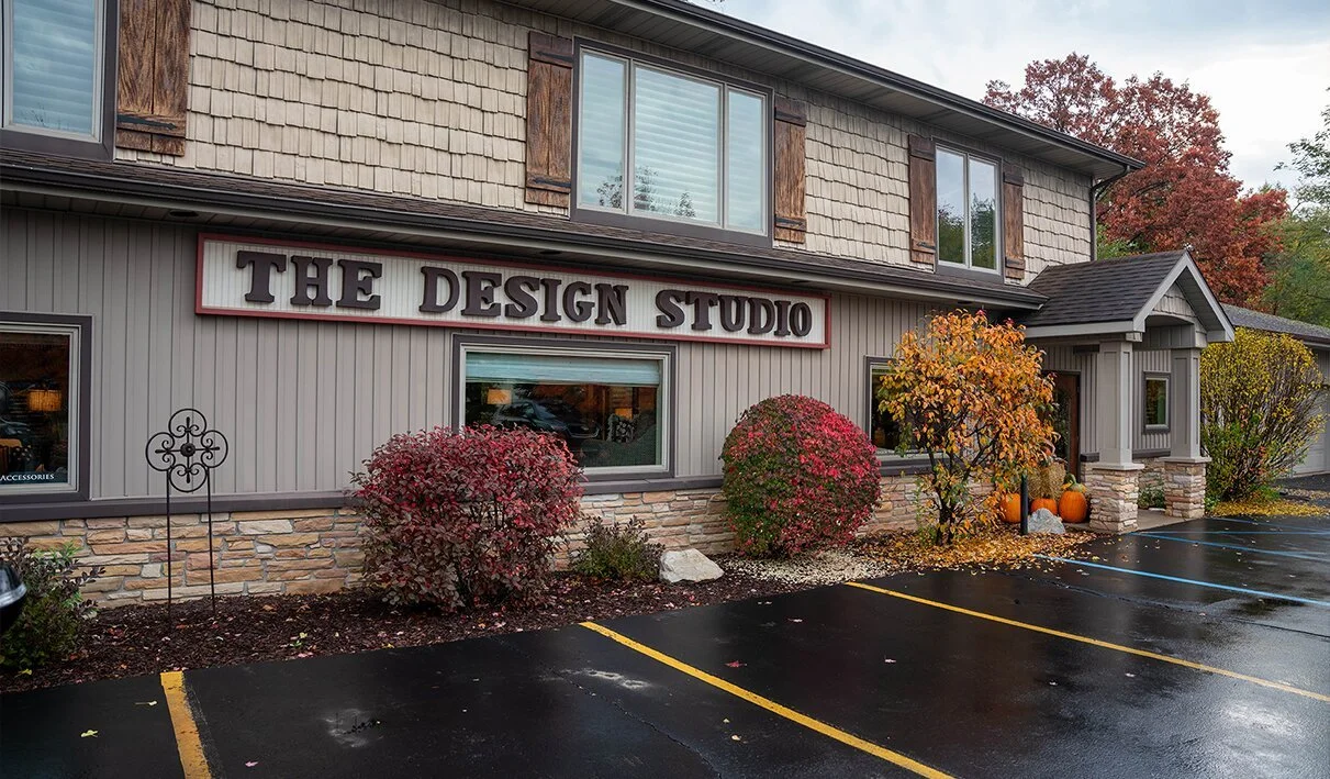 Exterior of a building labeled 'The Design Studio' with fall foliage, bushes, pumpkins, and a wet parking lot.