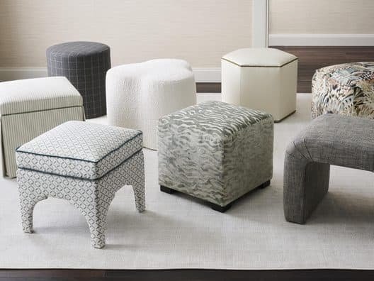 Living room with various patterned ottomans and a white sofa, dark hardwood floor, and yellow curtains.